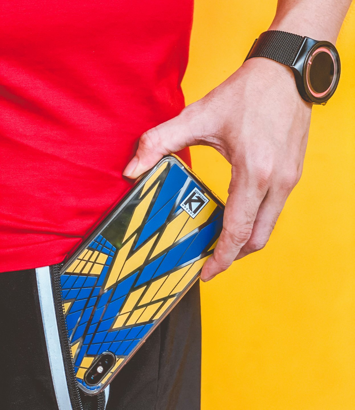 Une main glisse un smartphone à motif géométrique dans la poche d'un short de sport.