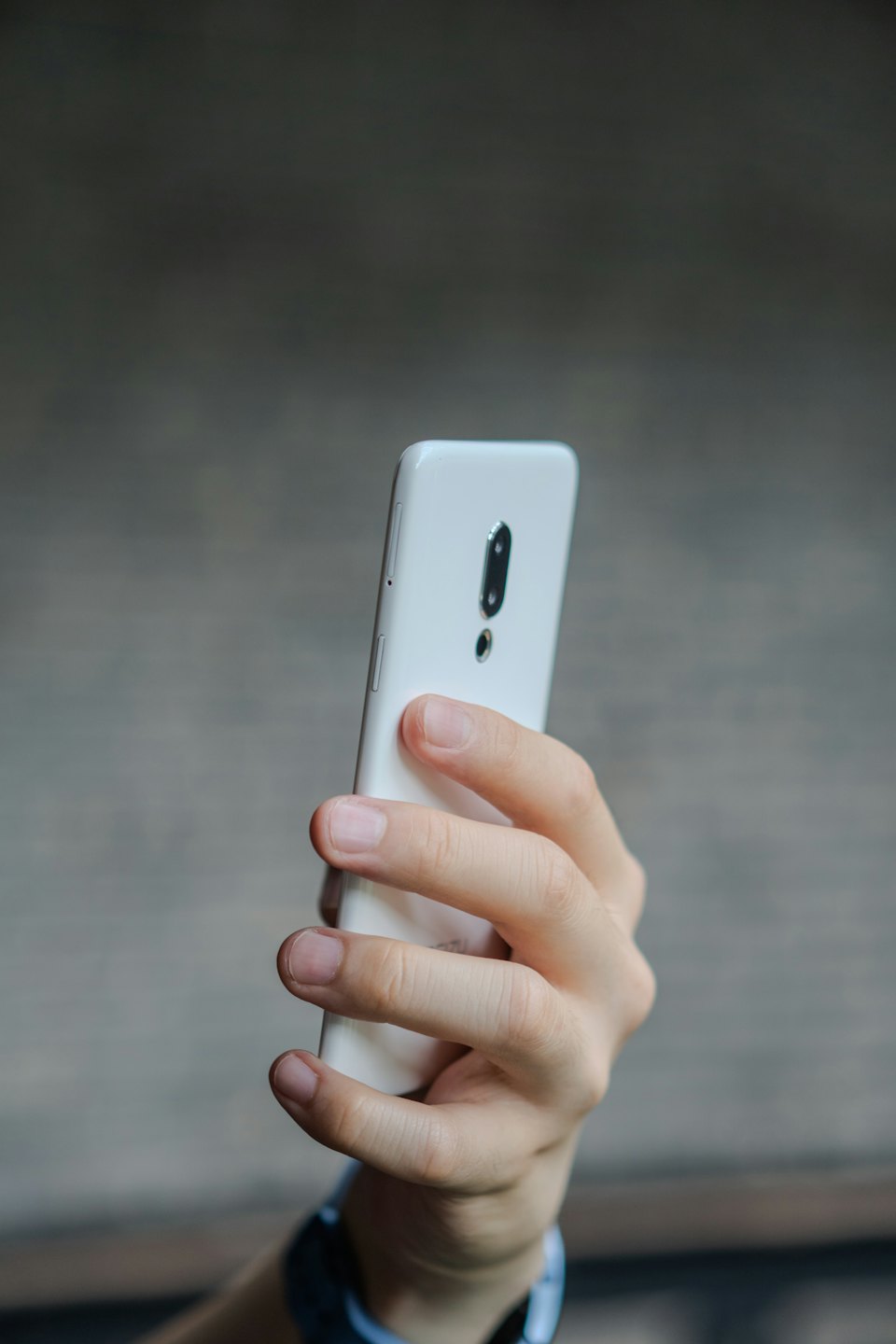 Une main tient un smartphone blanc avec un module caméra visible.
